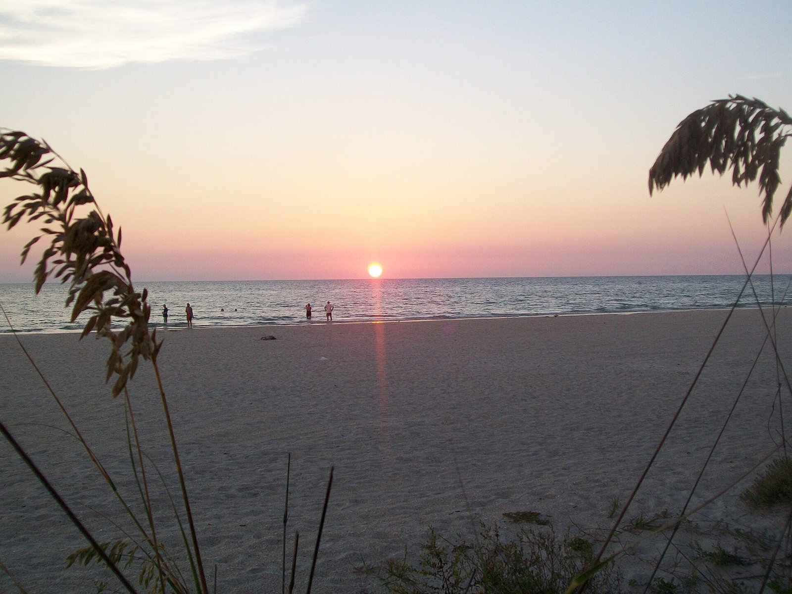 White sand and calm water on the Florida Gulf Coast at sunset, a few people wading near the shore